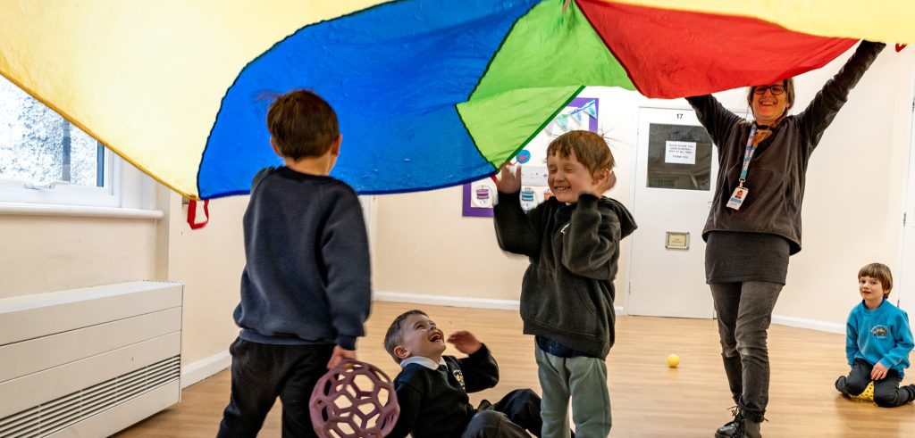 Children Playing Under A Rainbow Parachute