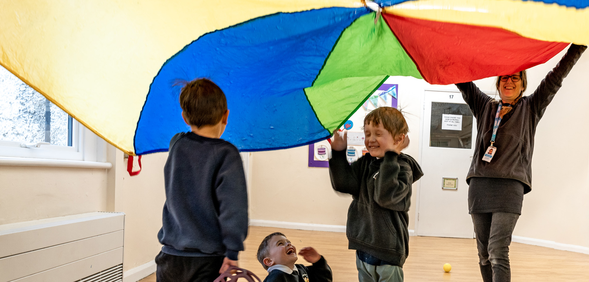 Children Playing Under A Rainbow Parachute